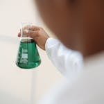 A scientist in a lab coat holding a flask with green liquid, focusing on scientific research.